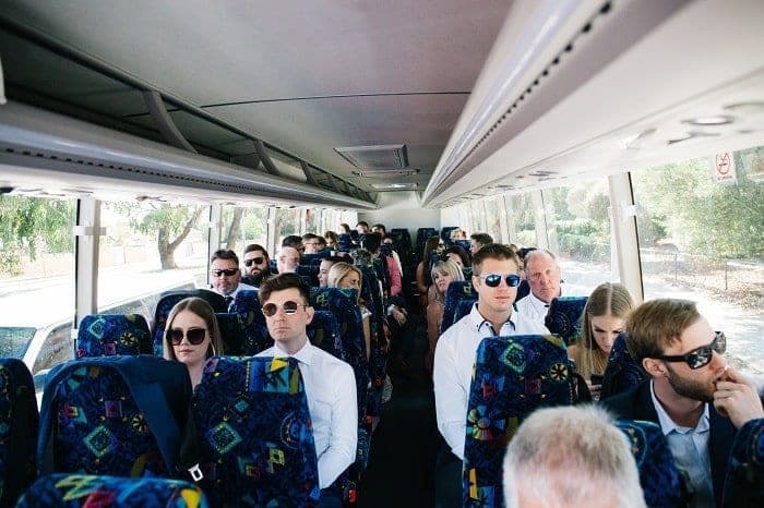 The interior of a Horizons West coach filled with wedding guests in suits and sunglasses, sunlight coming through the side windows