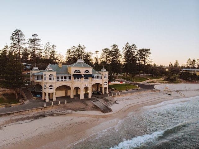 An aerial view of the Indiana Tea House on the sand at Cottesloe Beach at dusk, backed by a row of Norfolk Island pines
